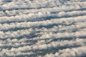 Windmills, windturbines above the fog clouds creating vortex trails