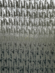 A close-up of a structured, grid-like surface with a repetitive pattern of raised, textured lines. The interplay of light and shadow highlights each line, creating a dynamic visual effect 