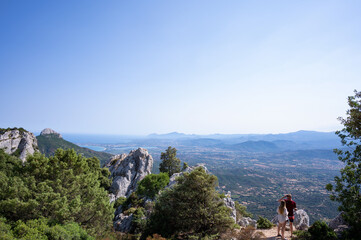 Hikers Enjoying Scenic Views in Sardinia Breathtaking Mediterranean Landscape. A stunning photograph capturing two hikers admiring the expansive views of Sardinias rugged landscape and Mediterranean