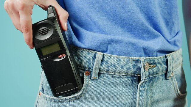 80s 90s retro vintage cell phone being used by a young adult woman, taking old mobile phone with antenna from jeans pocket.