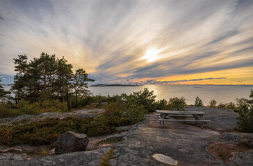 Obraz premium Wooden table and benches for tourists on the rocky seashore. Beautiful sunset sky. Photo