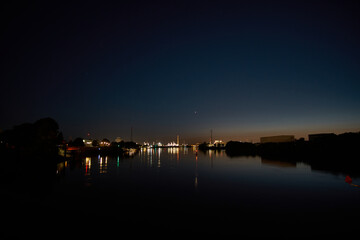 Fototapeta premium Evening calm over the tranquil river with city skyline illuminated by soft lights