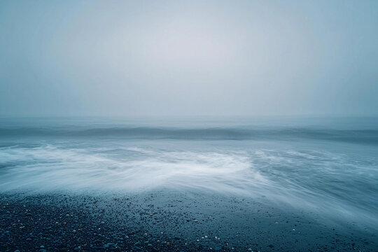 Calm sea waves gently rolling onto a rocky shore during foggy morning