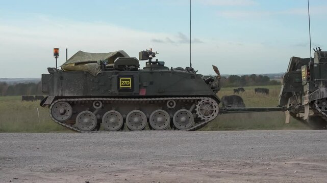 a British army Warrior FV512 MRV  towing a Bulldog FV432 a convoy of Warrior FV510 and Bulldog FV432 armoured personnel carrier tracked tanks on a dusty road