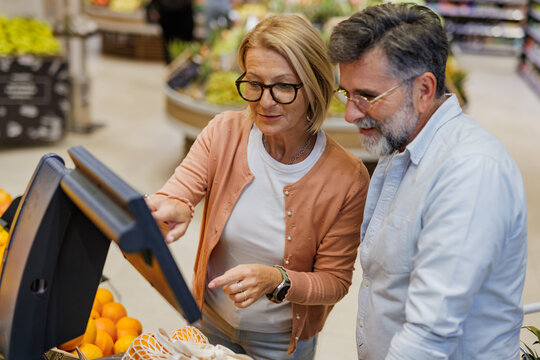Senior couple using self checkout kiosk in supermarket