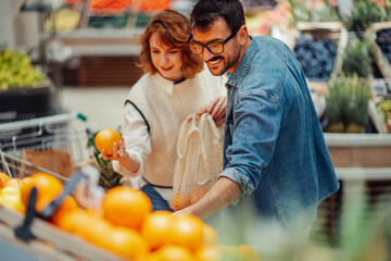 Couple buying oranges at grocery store using reusable bag