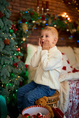 Cute Surprised little boy in Anticipation of Miracles and Holidays in a beautifully decorated Christmas room