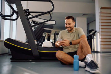 Happy athletic man texting on mobile phone in  gym.