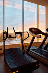 Curved treadmill next to gym window at sunset.
