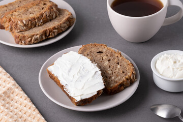 Slices of whole grain bread topped with cream cheese on a plate in a cozy kitchen setting