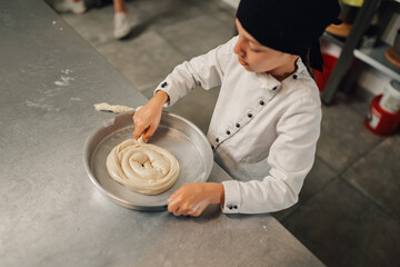 Fototapeta premium Young girl chef arranging dough spiral in baking tray for culinary process.