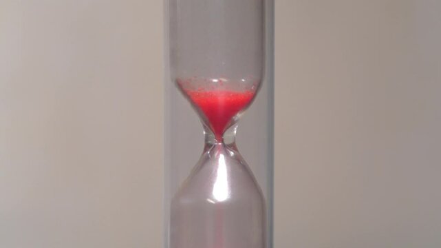 Red sand in hourglass. Time flows backwards, in the opposite direction. Time is like sand in the endless desert, but remember, your handful is in the hourglass. 4K 60fps macro shot reverse time video