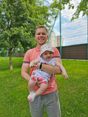 Fototapeta premium dad and a six-year-old baby are standing on the green grass and smiling at the camera. Child in arms