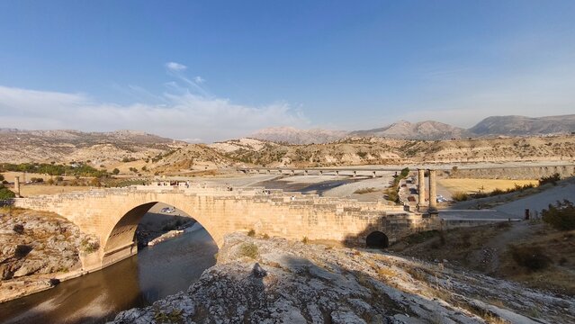Nemrut Cendere Bridge Ancient Roman bridge arches over a calm river against a backdrop of mountains. Historic Roman bridge in a mountainous landscape, showcasing ancient architecture and a tranquil

