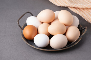A collection of fresh eggs displayed in a rustic bowl on a textured countertop with a soft cloth in the background