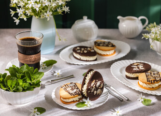 Delicious homemade cookies filled with cream decorated with chocolate and almonds on table setting for coffee break
