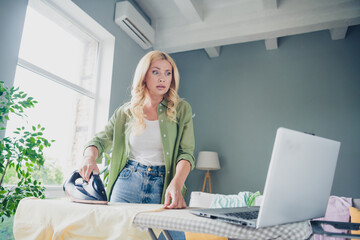 Mature woman multitasking at home, combining household chores and online tasks, dressed casually in...