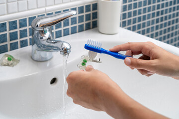 Close-up of hands cleaning a transparent dental retainer with a toothbrush under flowing water from a tap, highlighting oral hygiene and maintenance