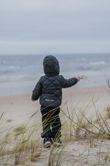 Small toddler girl in very warm grey winter nordic jacket and warm trousers throwing around handful...