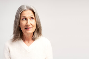 Excited, pensive senior woman looking away on copy space, posing isolated on white background