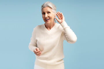 Portrait of smiling, beautiful senior woman having hearing aid in ear, isolated on blue background