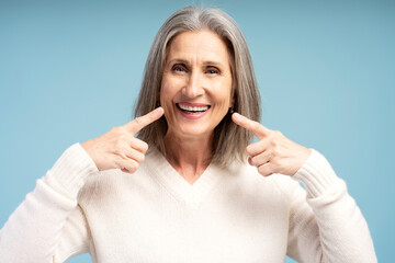 Portrait of smiling, beautiful senior woman pointing fingers on teeth smile, looing at camera