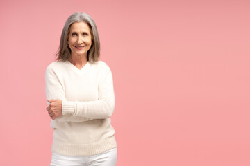 Fototapeta premium Smiling, senior, gray haired woman wearing white sweater, with crossed arms looking at camera