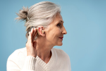 Profile, portrait of beautiful smiling gray haired woman having hearing aid in ear looking away © Maria Vitkovska