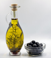 Transparent bottle of olive oil with herbs and seeds closeup.
