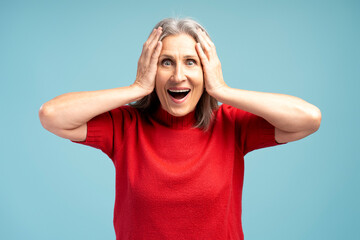 Excited, positive mature woman wearing red sweater with open mouth looking at camera