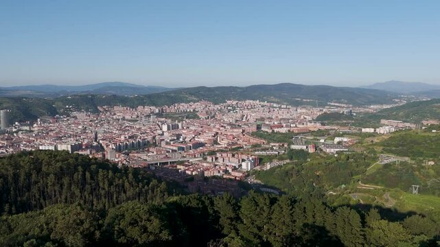 Aerial footage of the cityscape of Bilbao surrounded by green mountains in Biscay province, Spain