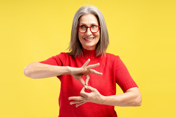 Smiling, gray haired senior woman wearing red sweater and stylish eyeglasses. Sign language concept
