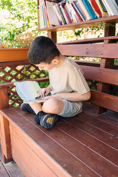 Boy Reading Book At Outdoor Library On Wooden Bench