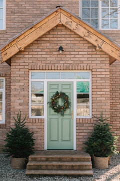 Green front door on brick house with festive wreath