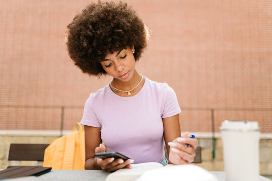 Girl with afro hair juggling phone and study.