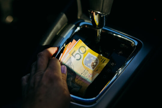 A hand holding Australian money  inside a car.