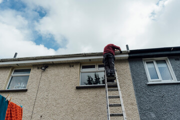 Man Fixing Gutters on a Ladder