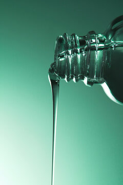 Water pouring from a clear glass bottle on gradient green background