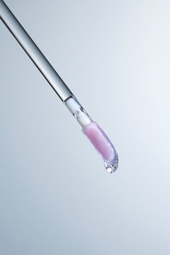 Purple lip gloss brush close up with a liquid droplet flowing down