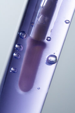 Lip gloss brush in purple liquid with air bubbles close up. 