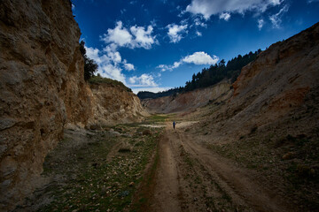 Vast canyon landscape with a lone hiker exploring the rugged terrain under a dramatic sky