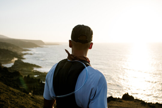 Runner with his back to camera admires sunset from top of a volcano
