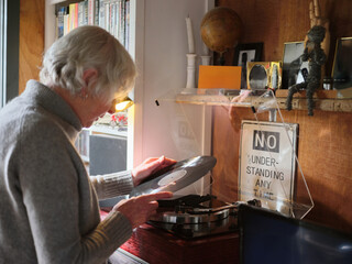 Senior woman at home playing vinyl records on turntable