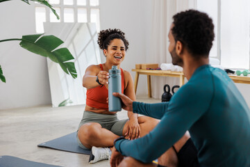 Happy couple sharing water bottle after training session at gym