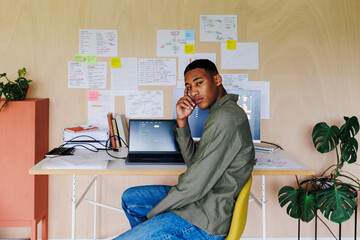Young programmer thinking about code sitting at desk in home office