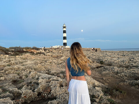 Woman admiring a lighthouse at dusk by the shore