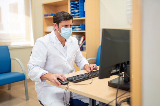Doctor working on computer in hospital office with mask