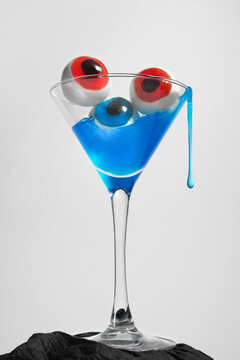 Blue cocktail with surreal eyeballs in a glass against a gray backdrop