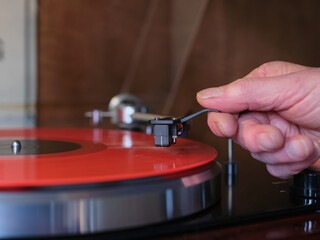 Hand placing needle on red vinyl record on middle track