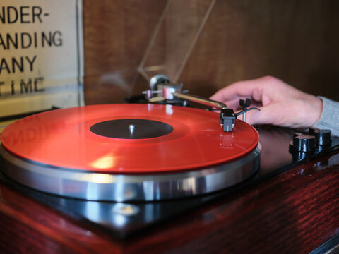 Hand placing needle on red vinyl record on turntable at home